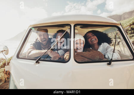 Friends on roadtrip smiling and laughing inside van. Group of man and women travelling together in an old minivan. Stock Photo