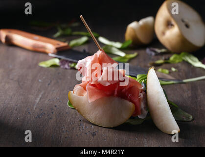Prosciutto with pear and spinach leaves on an old wooden table . Traditional Mediterranean snack . Stock Photo