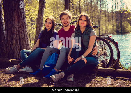 One male and two female relaxing in a park after riding with bicycles. Stock Photo