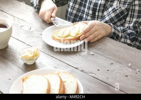 Male hands spreading butter on toasted bread while morning breakfast. Breakfast at home with bread, butter and tea. Stock Photo