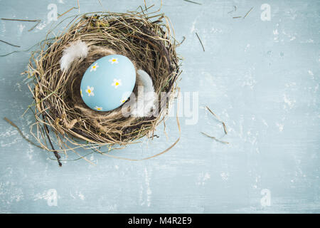 Easter Eggs in bird Nest on blue wooden background. Decorated easter eggs with feathers in nest on old wooden table with copy space. Spring, Easter or Stock Photo