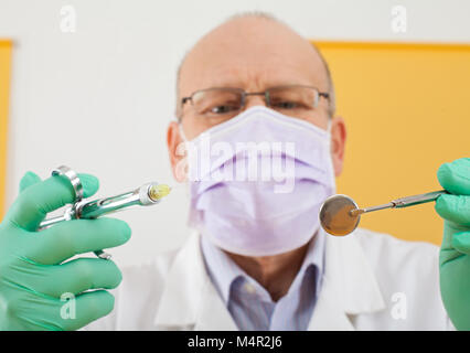 Close up picture of senior male dentist holding dental instruments - anesthesic syringe and mirror Stock Photo