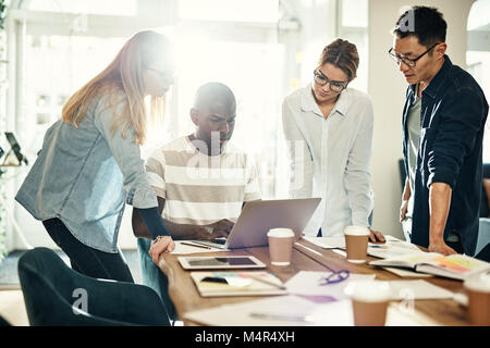 Diverse group of focused design professionals working over a laptop together at a table in a bright modern office Stock Photo