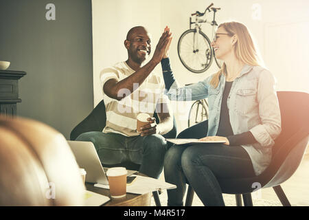 Two smiling young business colleagues sitting in a stylish modern office smiling and high fiving each other Stock Photo
