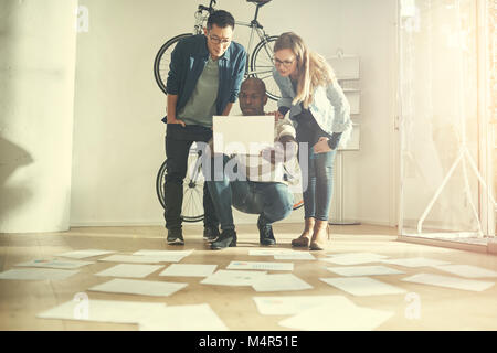 Diverse group of colleagues reading a document from paperwork spread out on the floor in front of them while working in a stylish modern office Stock Photo