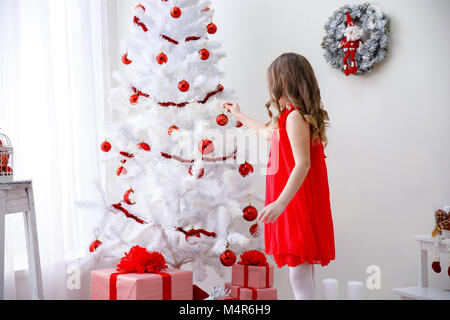 Adorable little girl with curly hair decorates a beautiful white  Christmas tree Stock Photo