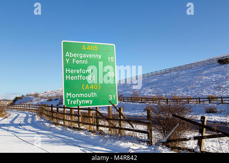 Road sign on the A465 with directional and milage information to Abergavenny, Hereford and Monmouth in winter with snowy conditions and blue sky. Stock Photo