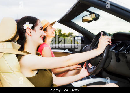 Close-up open interior of modern luxury sports roadster car with two young woman enjoying freedom and life style under clear sky on a summer sunny day Stock Photo