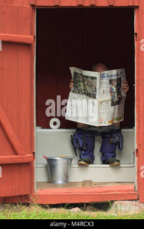 A man sitting and reading the newspaper on the privy Stock Photo