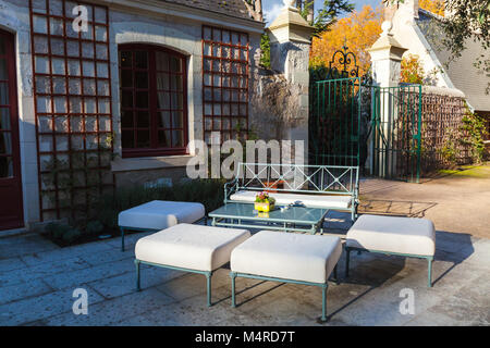 Outdoor furniture, bench and sofas stand around coffee table in autumn French park Stock Photo