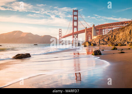 Classic panoramic view of famous Golden Gate Bridge seen from scenic Baker Beach in beautiful golden evening light at sunset, San Francisco, USA