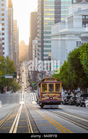 Classic view of historic Cable Car riding on famous California Street in beautiful golden morning light at sunrise in summer, San Francisco, USA