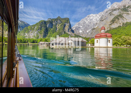 Classic view of traditional passenger boat gliding on Lake Konigssee with world famous Sankt Bartholomae pilgrimage church and Watzmann mountain Stock Photo