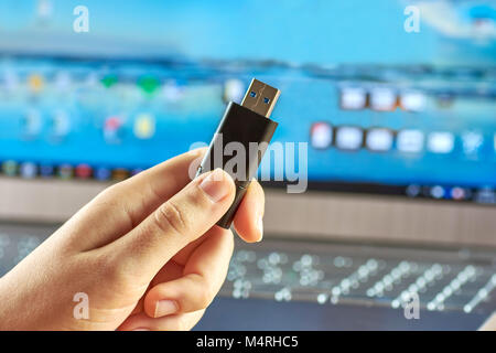 A female hand holding a USB flash drive before the silver laptop is turned on Stock Photo