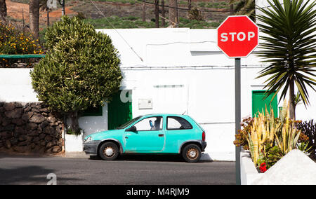 Colors of Lanzarote, a bright colored car parked in front of a typical white house with green doors with a stop sign in the village of Haría, Lanzarot Stock Photo