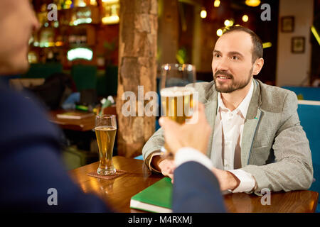 Two smiling business partners having informal meeting in pub: they drinking beer and discussing details of mutually beneficial cooperation Stock Photo