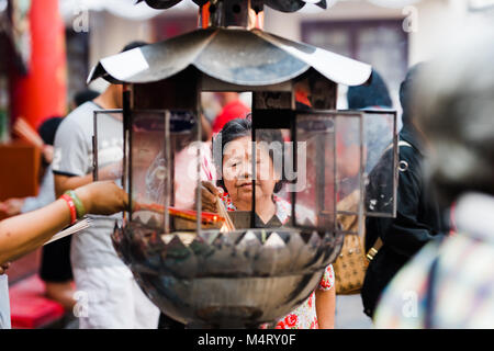 BANGKOK, THAILAND - FEBRUARY 18, 2018: A woman lights incense during Chinese New Year at a temple in Bangkok's Chinatown. Stock Photo