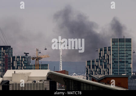 London, UK. 18th Feb, 2018. London Fire: Black smoke rises over buildings from east London with Emirates airline cable cars in view. Credit: Guy Corbishley/Alamy Live News Stock Photo