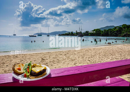 Plate of cheeseburger and salad set on fuschia pink bench on Honeymoon Beach, Water Island, US Virgin Islands. Stock Photo