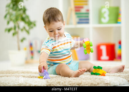 Happy baby playing with colorful plastic bricks on the floor. Toddler having fun and building a train out of constructor bricks. Early learning. Developing toys Stock Photo