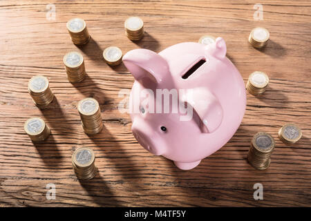 Elevated View Of A Piggybank Surrounded With Coin Stacks On Wooden Table Stock Photo