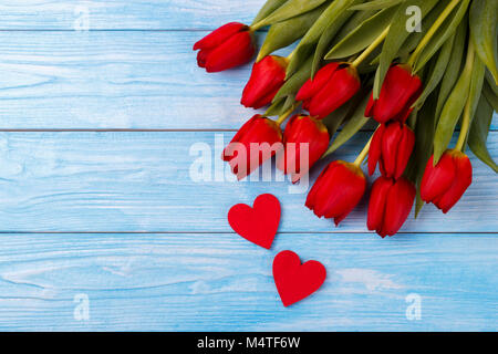 Red tulips and two wooden hearts over blue wooden background, overhead view with copy space Stock Photo
