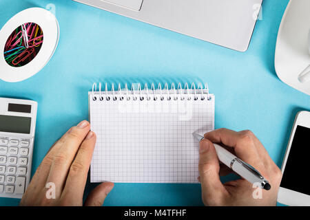 Close-up Of A Businessman Writing On Checkered Spiral Notepad Over The Office Desk Stock Photo