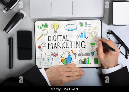 Close-up Of A Businessperson Drawing Digital Marketing On Notebook Over The Office Desk Stock Photo