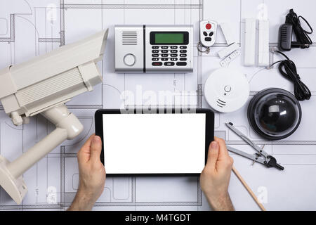 Close-up Of A Person Holding Blank Screen Digital Tablet On Blueprint With Security Equipments Stock Photo