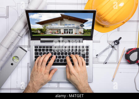 Close-up Of A Architect Using Laptop With A House On Screen Over The Blueprint Stock Photo