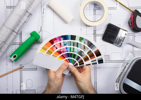 Architect Holding Color Guide Swatch On Blueprints With Paint Roller And Paint Brush Stock Photo