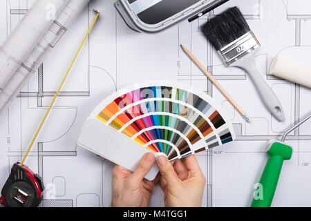 Architect Holding Color Guide Swatch On Blueprints With Paint Roller And Paint Brush Stock Photo