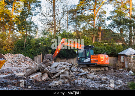 Construction site with orange heavy plant tracked mechanical excavator: remains of the demolition of a residential house prior to redevelopment Stock Photo