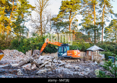 Construction site with orange heavy plant tracked mechanical excavator and skip: remains of demolition of a residential house prior to redevelopment Stock Photo