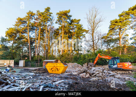Construction site with orange heavy plant tracked mechanical excavator and skip: remains of demolition of a residential house prior to redevelopment Stock Photo