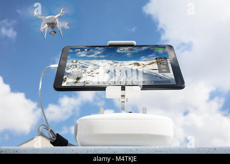Low angle view of drone filming mountains seen on tablet computer against cloudy sky Stock Photo