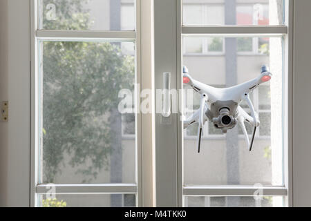 Flying white quadrocopter spying through window of a house Stock Photo