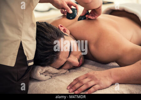 Man relaxing under the stimulating effects of a traditional hot stone massage Stock Photo