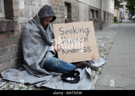 Male Beggar In Hood Showing Seeking Human Kindness Sign On Cardboard Stock Photo