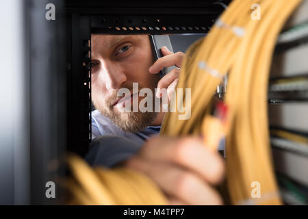 Technician Talking On Mobile Phone While Working In Server Room Stock Photo