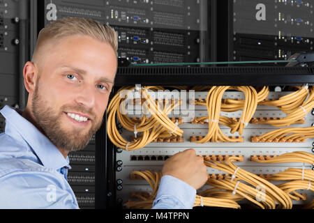 Portrait Of A Smiling Young Computer Technician Checking The Server Cables In Data Center Stock Photo