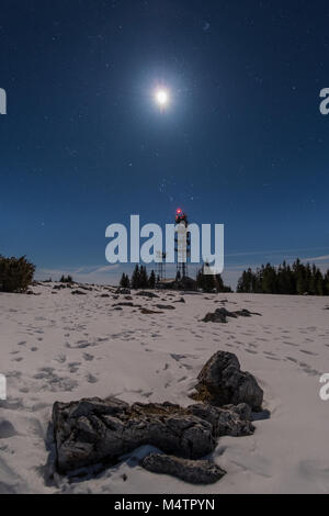 Transmitter station tower on snow covered mountain Schoeckl with moon and stars in the sky Stock Photo