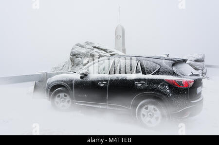 Black family car on snowy mountain peak. Frosty wintry scene with the sport utility vehicle standing inside cloud at the top of the hill in mountains. Stock Photo
