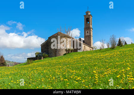 Old medieval church on the meadow with green grass and yellow flowers under blue sky in Piedmont, Northern Italy. Stock Photo