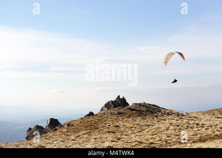 Sky diver floating in the air over grass covered mountain landscape Stock Photo