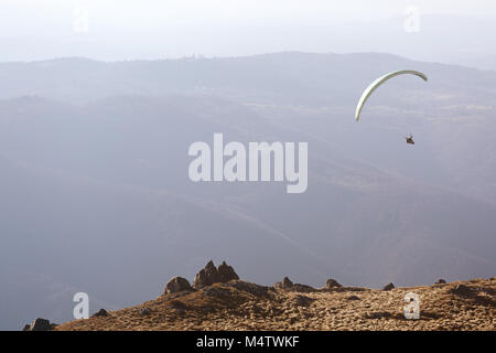 Sky diver floating in the air over grass covered mountain landscape Stock Photo