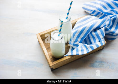 Milk in vintage bottles with stripped blue and white straws in wooden box on white rustic table with copyspace Stock Photo