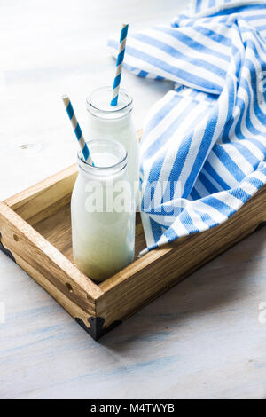 Milk in vintage bottles with stripped blue and white straws in wooden box on white rustic table with copyspace Stock Photo