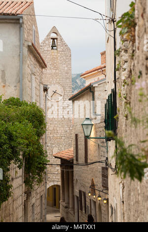 Narrow alleyway in Rab old town with clock / bell tower and houses built of white bricks and red roof tiles Stock Photo