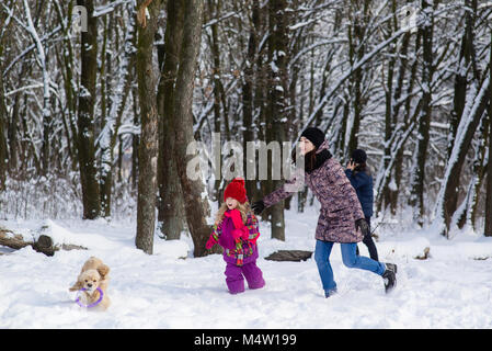 Family run in snow after their dog with purple toy Stock Photo